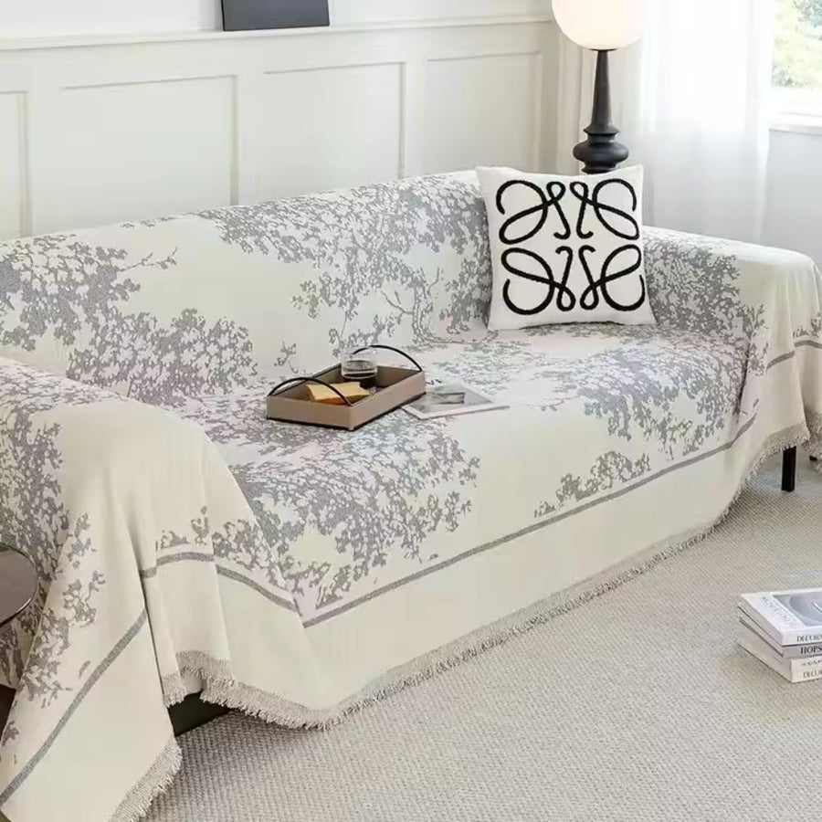 Chenille floral sofa cover in warm taupe draped casually over a modern sofa in a cozy, sunlit living room