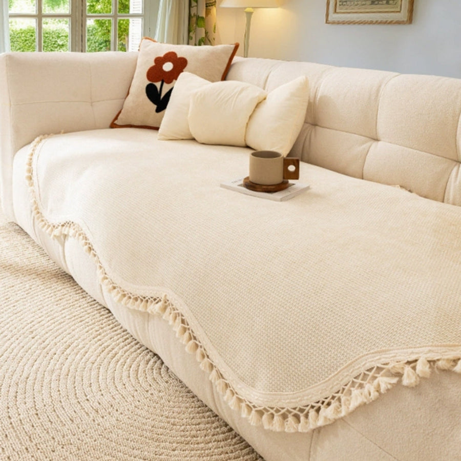 Cream chenille woven sofa cover with tassel edges draped over a neutral linen sofa in a warm-toned living room