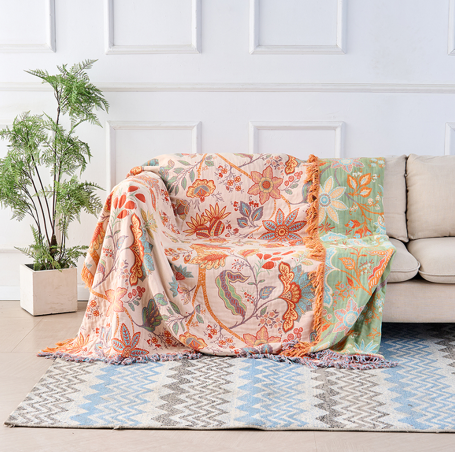 Boho floral cotton throw blanket in cream with orange and blue tapestry print draped over a sofa