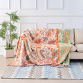 Boho floral cotton throw blanket in cream with orange and blue tapestry print draped over a sofa