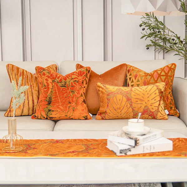 Multiple orange velvet pillow covers in assorted sizes arranged together on a bed with neutral bedding