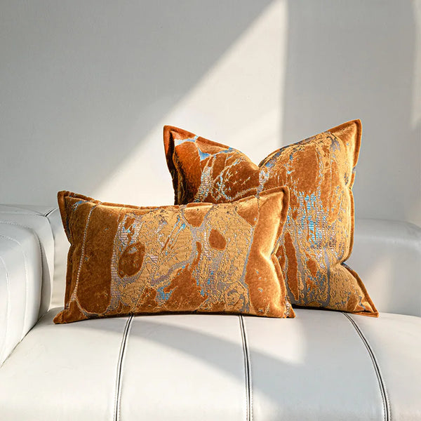 Styled bedroom scene with orange jacquard pillow cover layered among neutral cushions